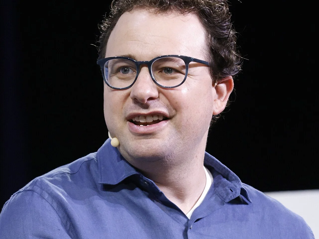 Dario Amodei i blå skjorta och glasögon talar på scen under TechCrunch Disrupt 2023